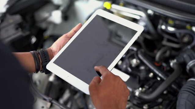 Close-up of an Asian male mechanic hand using special digital tablet used for car inspection and repairing damaged car parts. Car service and maintenance. Automotive check concept