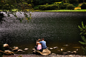 Romantic holiday. Young loving couple sitting together on a stone bank enjoying a beautiful lake.