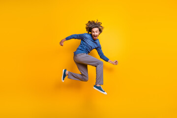 Fototapeta na wymiar Full length photo of excited positive man wear blue sweater jumping high having fun isolated yellow color background