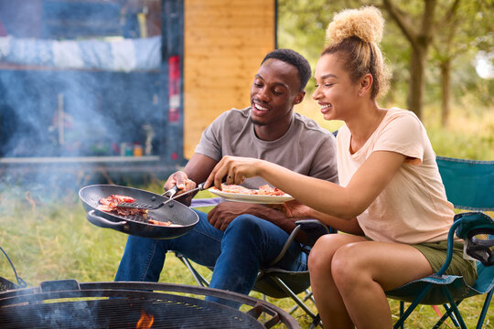 Couple Camping In Countryside With RV Cooking Bacon And Eggs For Breakfast Outdoors On Fire
