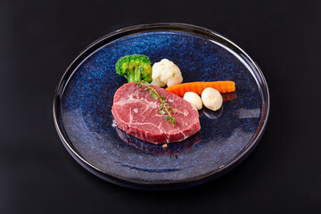 Raw Paleron (Oyster blade) with vegetable (Broccoli, cauliflower, garlic) top with Himalayan salt and thyme leaves on plate isolated on black background. Prepare beef and vegetables for cooking.