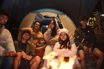 Group of multiethnic Asian friends gathered around bonfire smiling at camera 
