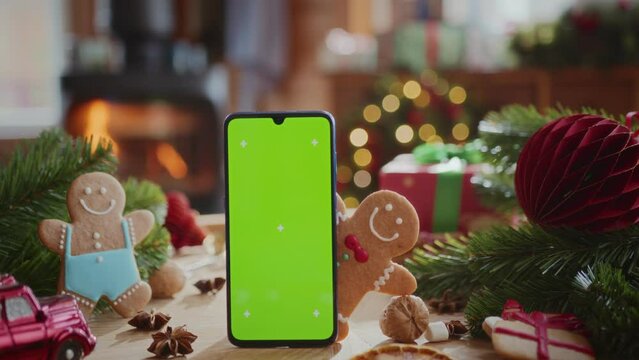 smartphone with green screen chroma key display with motion trackers on table with fir tree branches, gingerbread men and christmas decoration. burning fireplace and flashing lights on background