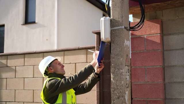 man checks the meter reading electricity in the cottage. An electrical engineer inspects a transformer box and makes entries in a log.