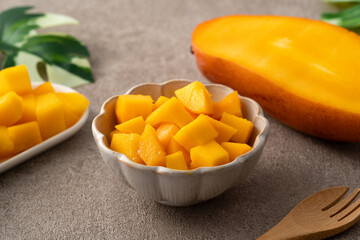 Fresh chopped, diced mango cubes on gray table background with tropical leaf.