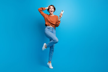 Full body photo of pretty young girl hold telephone amazed sales hold device wear trendy brown outfit isolated on blue color background - obrazy, fototapety, plakaty