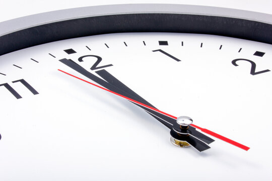 Midnight is coming. Black and white office clock with a red pointer on a gray background.