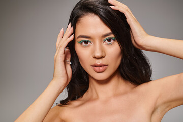 Fototapeta premium brunette asian woman with sparkling green eye makeup and bare shoulders posing on grey background