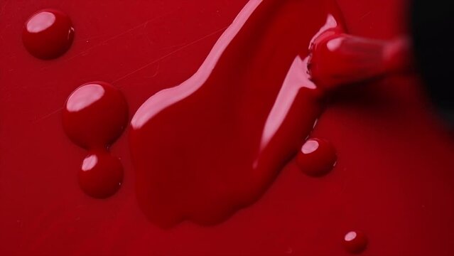 Red nail polish drops, manicure concept. Spilled uv gel, enamel, varnish with brush on red color background, splash. Beauty salon, nail care product. Nail art. Top view, fashion backdrop. Slow motion 