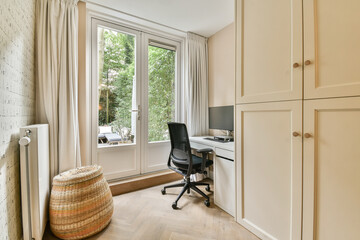 a room with a desk, chair and computer on the floor in front of a window that looks out onto trees
