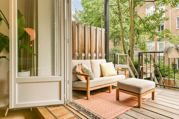 an outside area with a couch and chair on the deck looking out onto the trees in the yard behind it - obrazy, fototapety, plakaty