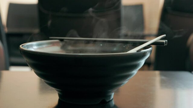 hot Thai beef noddle with meet balls in the black bowl with white smoke.  

