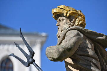 Partial view to an old sculpture of neptune and his  trident in front of the blue sky.