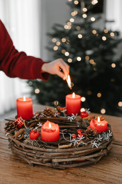 Female hand lighting all four candles on advent wreath on Christmas Eve. Celebrating cozy winter time at home.