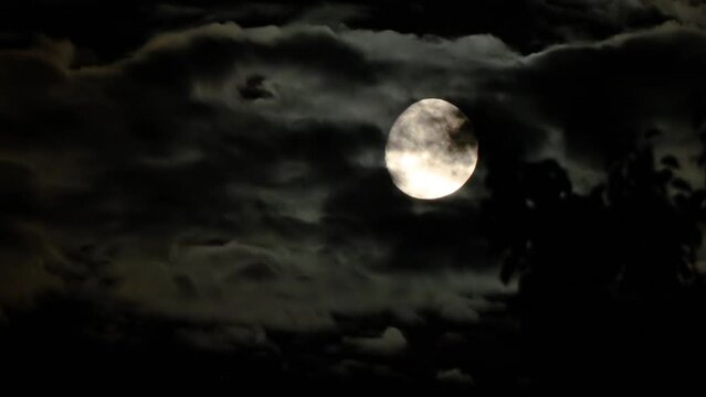 Moon on a dark cloudy night with natural clouds flying in front of the Moon like in thrillers and horror movies. Real shooting black clouds in the sky
