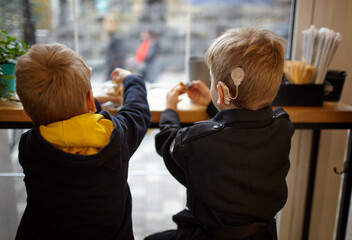 Boy have a Hearing Aids. Two twin brothers in a cafe. Selective focus, shallow depth of field - obrazy, fototapety, plakaty