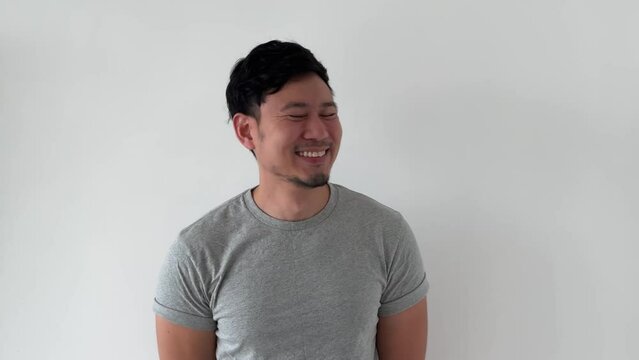 Happy laughing asian man wears grey t-shirt casual looking stand on white wall.