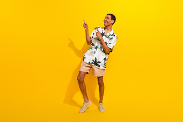 Fototapeta na wymiar Full size photo of handsome young guy point look empty space wear trendy palms print outfit isolated on yellow color background