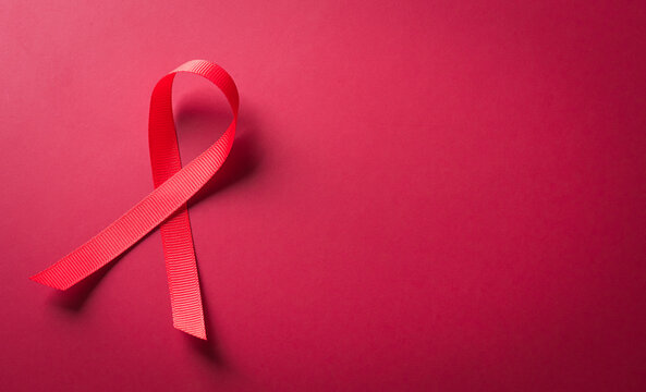 Closeup red ribbon HIV, world AIDS day awareness ribbon on red background. Healthcare and medicine concept.