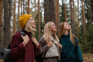 The girls travel on foot through an autumn forest. Happy camper friends walking along the dirt road to the campsite