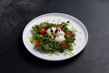 Salad with arugula, tomato and burrata cheese on a dark background.