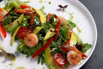 Salad with arugula, tomato, avocado and shrimp on a dark background.
