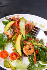 Salad with arugula, tomatoes, avocado and shrimp on a fork.