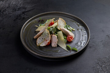 Salad with pieces of meat, tomatoes and cheese on a dark background.