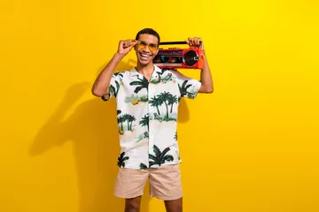 Fototapeten Photo portrait of handsome young guy hold tape recorder dancing wear trendy palms print outfit isolated on yellow color background © deagreez