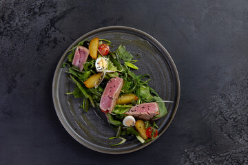 Salad with pieces of fried tuna on a dark background.