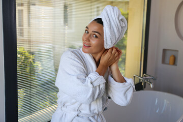 Portrait of beautiful mid adult woman in a bathroom wearing hair towel wrap and bathrobe after...