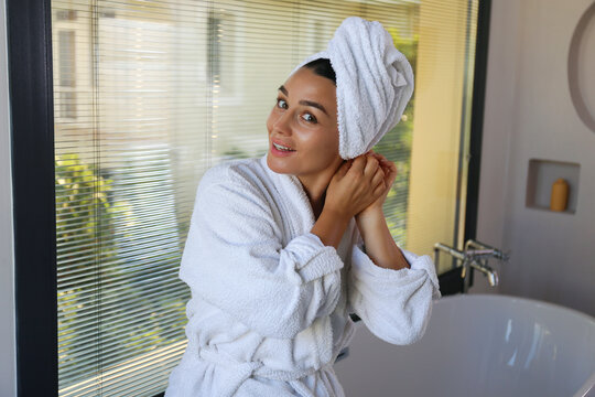 Portrait of beautiful mid adult woman in a bathroom wearing hair towel wrap and bathrobe after taking a bath. Self care concept. Close up, copy space background