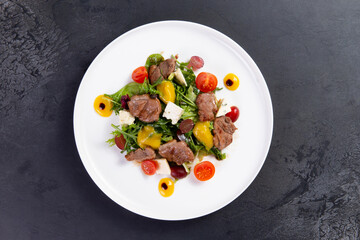 Salad with pieces of beef, tomato and cheese on a dark background.