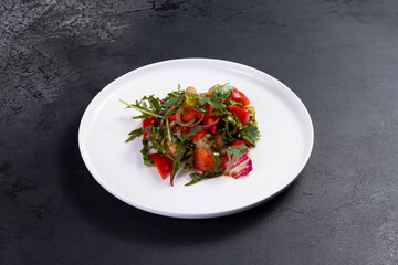 Salad with arugula, tomato and eggplant on a dark background.