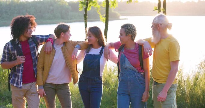 Symbols of friendship. Group of ethnically diverse people standing arm to arm in the middle of a meadow, throwing their joint hands in the air. Equality among people. High quality 4k footage