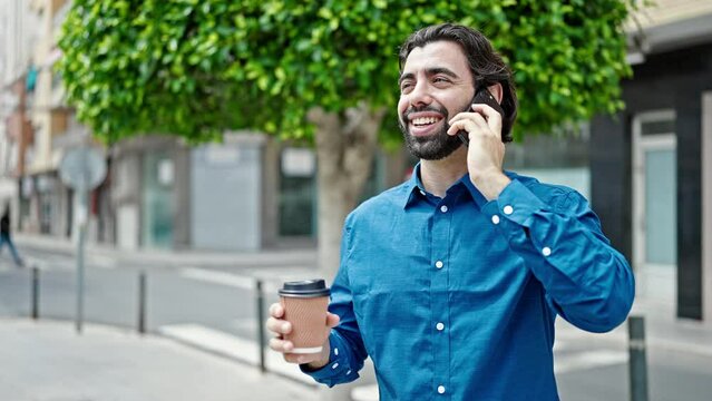 Young hispanic man talking on smartphone drinking coffee at street