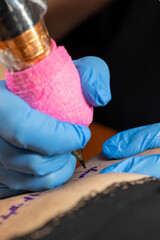 Cropped close up of a female tattoo artist working at his studio tattooing a string of text on the...