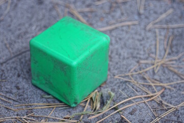 one green dirty square plastic cube toy lies on the gray sand on the street