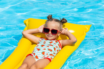 Cute little girl lying on inflatable mattress in swimming pool with blue water on warm summer day...