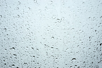 Closeup of rain drops on window on grey sky background