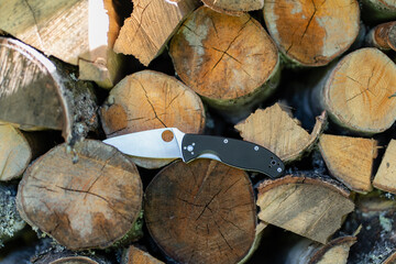 Folding knife next to firewood, survival knife. - obrazy, fototapety, plakaty