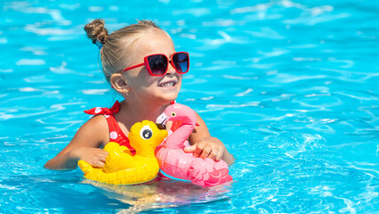 Little girl having fun on vacation at the hotel pool. Colorful vacation concept. Summer outdoor activity during family vacation in tropical resort. Beach and water toys. Sun protection.