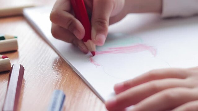 A preschool child draws with colored pencils in an album. Child's hand with a pencil close-up, selective focus. The girl draws a colored cloud