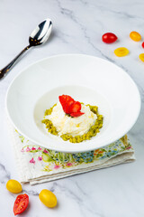 curd dessert with strawberries on top in a white plate on a marble background, side view