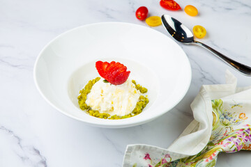 curd dessert with strawberries on top in a white plate on a marble background, side view