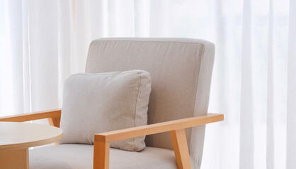 Gray cushion on armchair in front of white curtain inside of modern living room, beige tone style and home interior concept