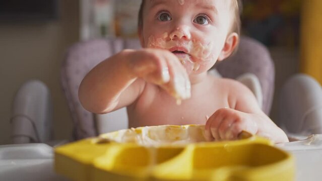 baby eats dirty. happy family a kid toddler concept. lifestyle baby girl dirty sitting messing with food at the table for feeding in the kitchen. grimy toddler in the kitchen