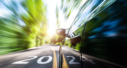 New year number 2024  and arrow sign on the road with car in motion blur driving to forest - obrazy, fototapety, plakaty
