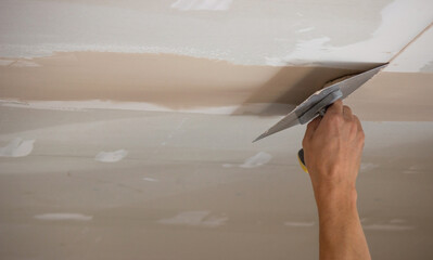 A man puts putty on a plasterboard ceiling. Putty for the joints of plasterboard sheets