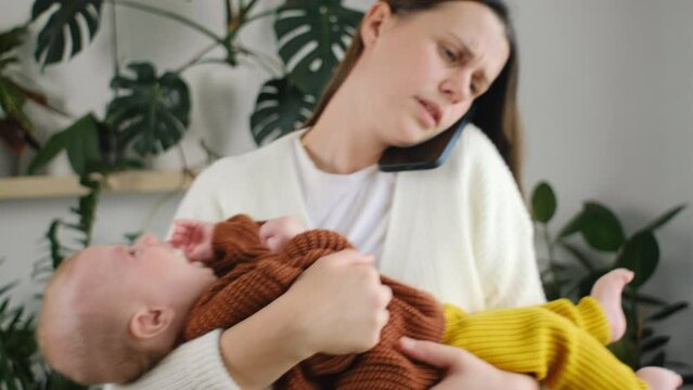 Worried Young Mother Holding Newborn Baby Son On Hands And Talking On Smartphone, Concerned Sad Millennial Mom Calling To Doctor To Get Advice About Infant Health And Child Care. Motherhood Concept